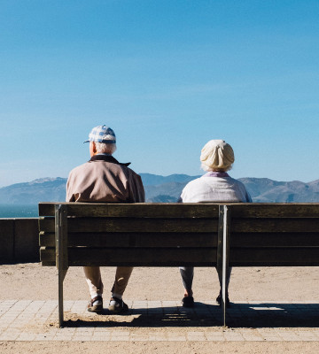 man and woman sitting on bench facing sea