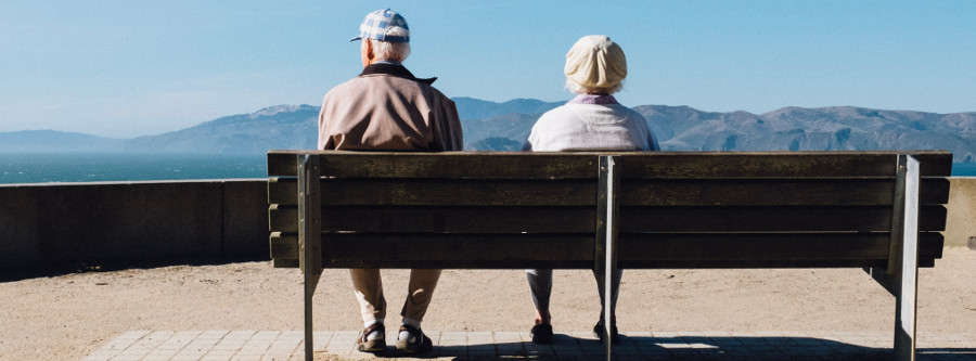 man and woman sitting on bench facing sea